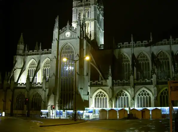Bath Abbey illuminated at night with chalet roofs below